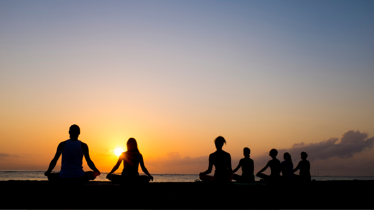 Silhouettes of a group meditating cross-legged on a beach at sunset